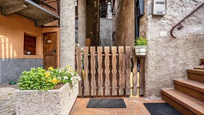 Een smalle steeg met een houten poort, een stenen plantenbak met bloemen en een betegelde entree.