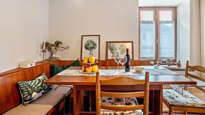 Een eetgedeelte met een houten tafel, stoelen, een bank en een raam met gordijnen.
