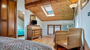 Een slaapkamer met een houten plafond, een bed, een kapstok, een rieten stoel en een dakraam.