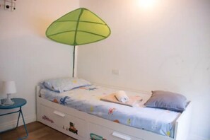 A small, single-bed room with a green umbrella-shaped lamp, a bedside table with a lamp, and a bed with a colorful blanket and pillows. - My Heart in Argegno - My Home in Como (Argegno)