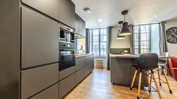 Une cuisine moderne dotée d’appareils électroménagers intégrés, d’un plancher en bois et d’un coin repas avec une chaise et une table.