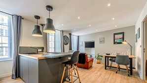 Une cuisine moderne avec un îlot central, des tabourets de bar, une table à manger avec des chaises, un téléviseur et une horloge au mur.