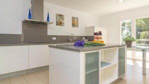 Une cuisine moderne avec des meubles blancs, un îlot central et une fenêtre donnant sur la verdure.