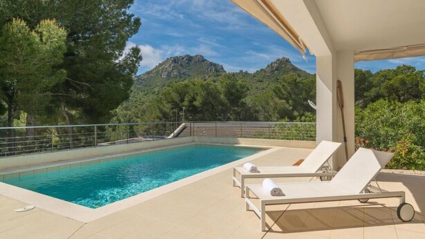 Une piscine entourée d’arbres et de montagnes, avec des chaises longues à proximité.
