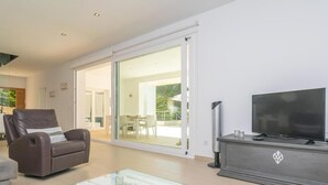 Un salon moderne avec un canapé, une table basse en verre, un téléviseur à écran plat et une porte-fenêtre coulissante donnant sur un balcon.