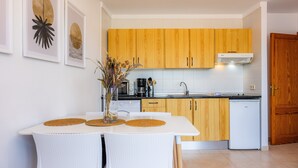 Een moderne keuken met houten kastjes, een wit aanrechtblad en een zithoek met een witte tafel en stoelen.