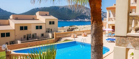 Una piscina amb vistes al mar i a les muntanyes, envoltada d'edificis amb balcons.