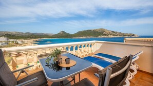 Een balkon met een tafel, stoelen en uitzicht op zee en bergen.