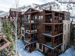 A multi-story wooden building with balconies, a stone facade, and a ski lift in the background.