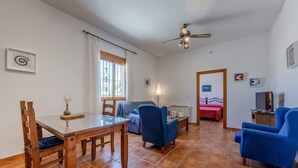Een ruime woonkamer met een eettafel, blauwe stoelen, een bank en een plafondventilator.