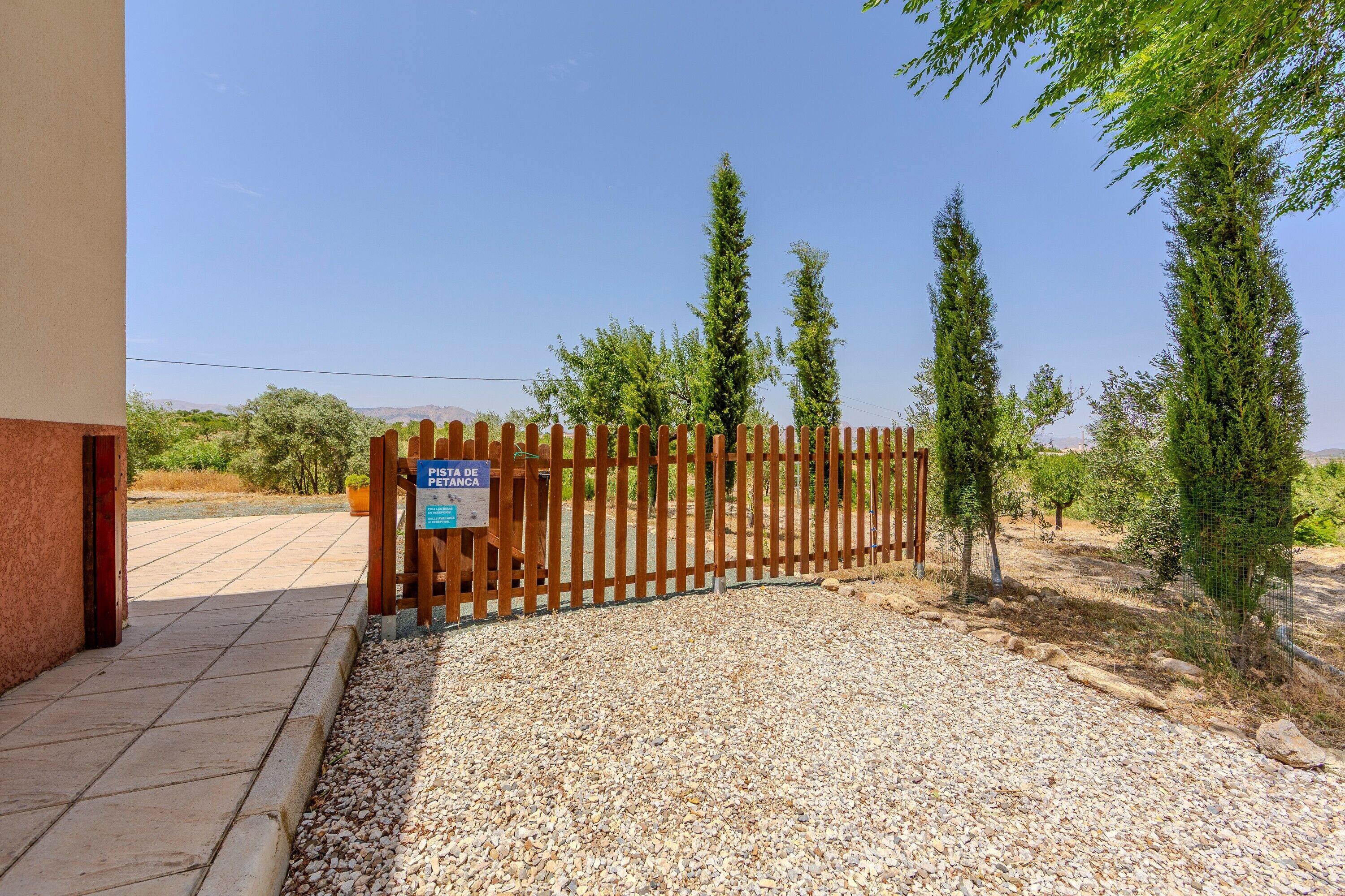 A gated entrance with a sign, gravel path, and trees.