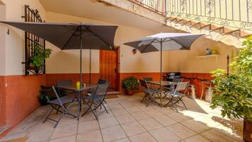 Un patio al aire libre con mesas, sillas, sombrillas, plantas en macetas y una escalera.
