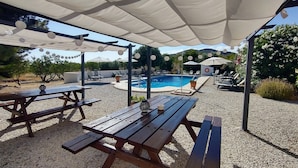 A covered outdoor area with a pool, wooden tables, and lounge chairs.
