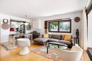 A modern living room with a glass coffee table, a leather sofa, and a dining area with a wooden table and chairs.