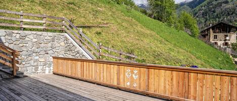 A wooden deck with a stone wall and a wooden railing.
