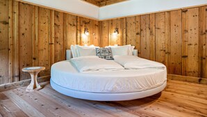 Ein rundes Bett in einem Raum mit Holzwänden und -decke, ein kleiner Nachttisch und zwei Wandleuchten.