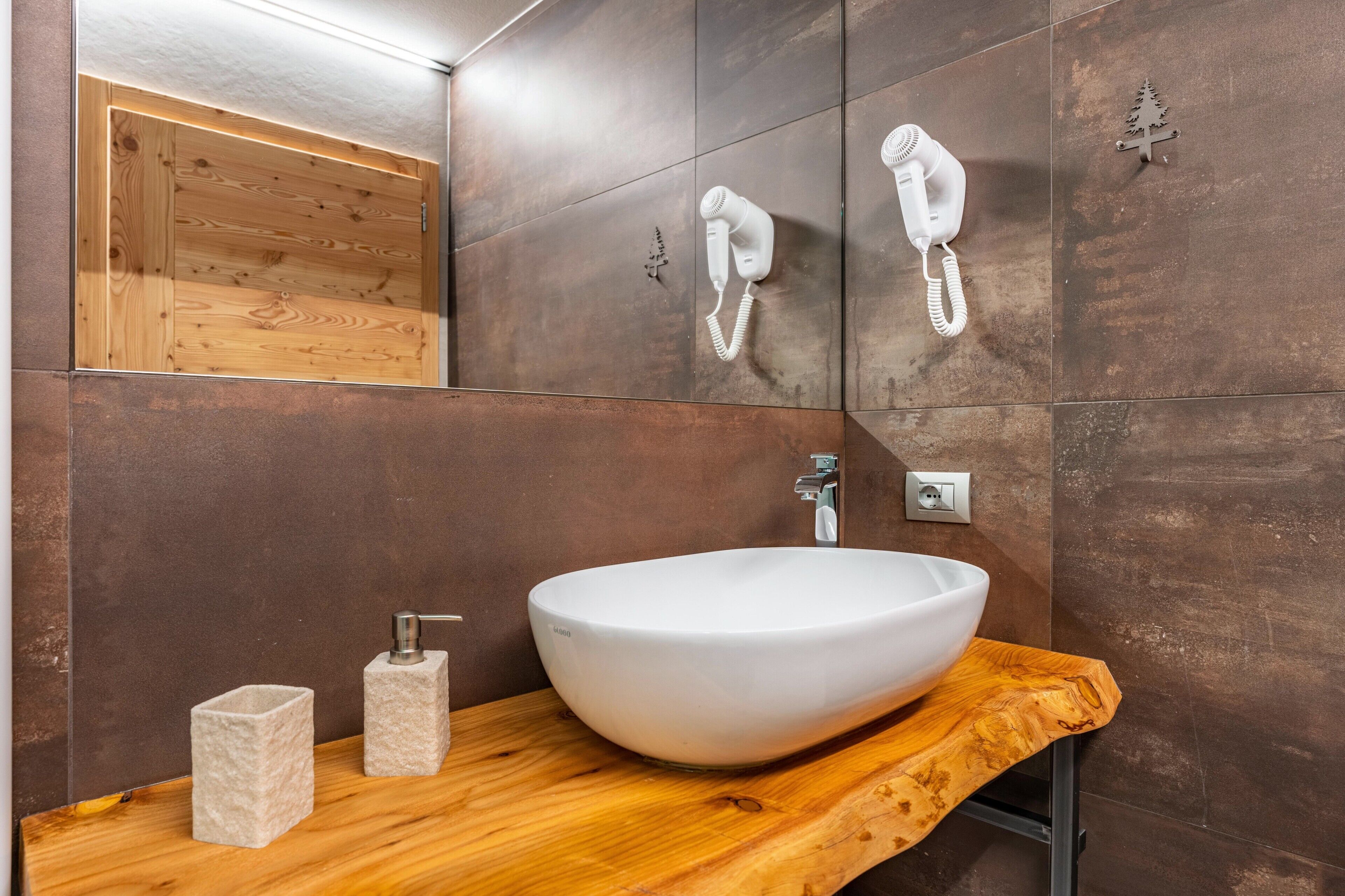 Un baño moderno con un lavamanos blanco de diseño, tocador de madera y dos secadores de pelo montados en la pared.