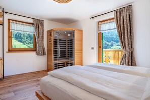 A bedroom with a large bed, wooden wardrobe, and a view of a forest through a window.
