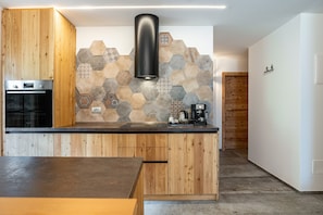 Una cucina moderna con mobili in legno, forno integrato, pannelli posteriori in piastrelle esagonali e cappa aspirante nera.