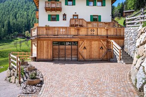A traditional chalet with a wooden balcony, stone staircase, and a paved driveway.