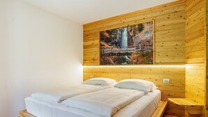 A double bed in a room with wooden walls and a painting of a waterfall.
