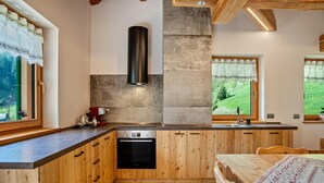 A kitchen with wooden cabinets, a built-in oven, and a window with a view of greenery. - 'Volo Dell'aquila' Apartment with Private Sauna and Mountain Views (Rabbi)