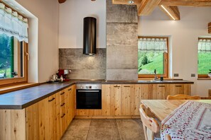 Une cuisine avec des meubles de rangement en bois, un four encastré et une fenêtre donnant sur un paysage verdoyant.