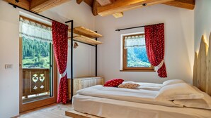 A room with a wooden bed, a window with a view of a forest, and a door with a view of a valley. - 'Volo Dell'aquila' Apartment with Private Sauna and Mountain Views (Rabbi)