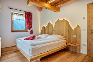 A wooden bed with a headboard, a window with a view, and a wooden floor.