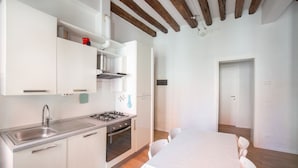 Una cocina moderna con armarios blancos, un lavamanos de acero inoxidable y una estufa a gas. En la habitación contigua hay una mesa de comedor con sillas.