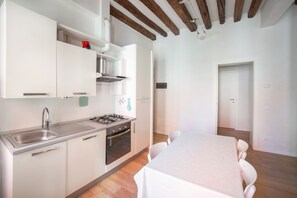 A modern kitchen with white cabinets, a stainless steel sink, and a gas stove. There is a dining table with chairs in the adjacent room. - Ca Lion, next Biennale (Venice)