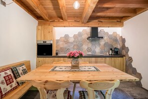 A wooden dining table with chairs, a kitchen with hexagonal tiles, and a wooden ceiling. - Apartment 'Whisper of the Stream' with Mountain View, Shared Garden and Wi-Fi (Rabbi)