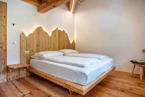 A wooden bed with a headboard, a bedside table, and a small stool. - Apartment 'Whisper of the Stream' with Mountain View, Shared Garden and Wi-Fi (Rabbi)