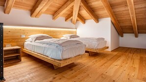 A bedroom with a sloped ceiling, wooden beams, a bed with white bedding, and a wooden nightstand. - Apartment 'Whisper of the Stream' with Mountain View, Shared Garden and Wi-Fi (Rabbi)