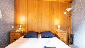 Une chambre à coucher avec une tête de lit en bois, deux tables de chevet avec des lampes, un lit avec deux oreillers et une couverture bleue.