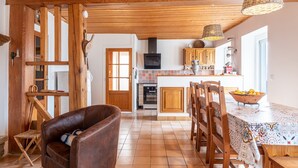 Une cuisine avec des meubles de rangement en bois, une table à manger avec des chaises et un luminaire suspendu.
