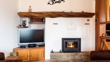 A living room with a fireplace, television, wooden shelves, and a stone fireplace surround.