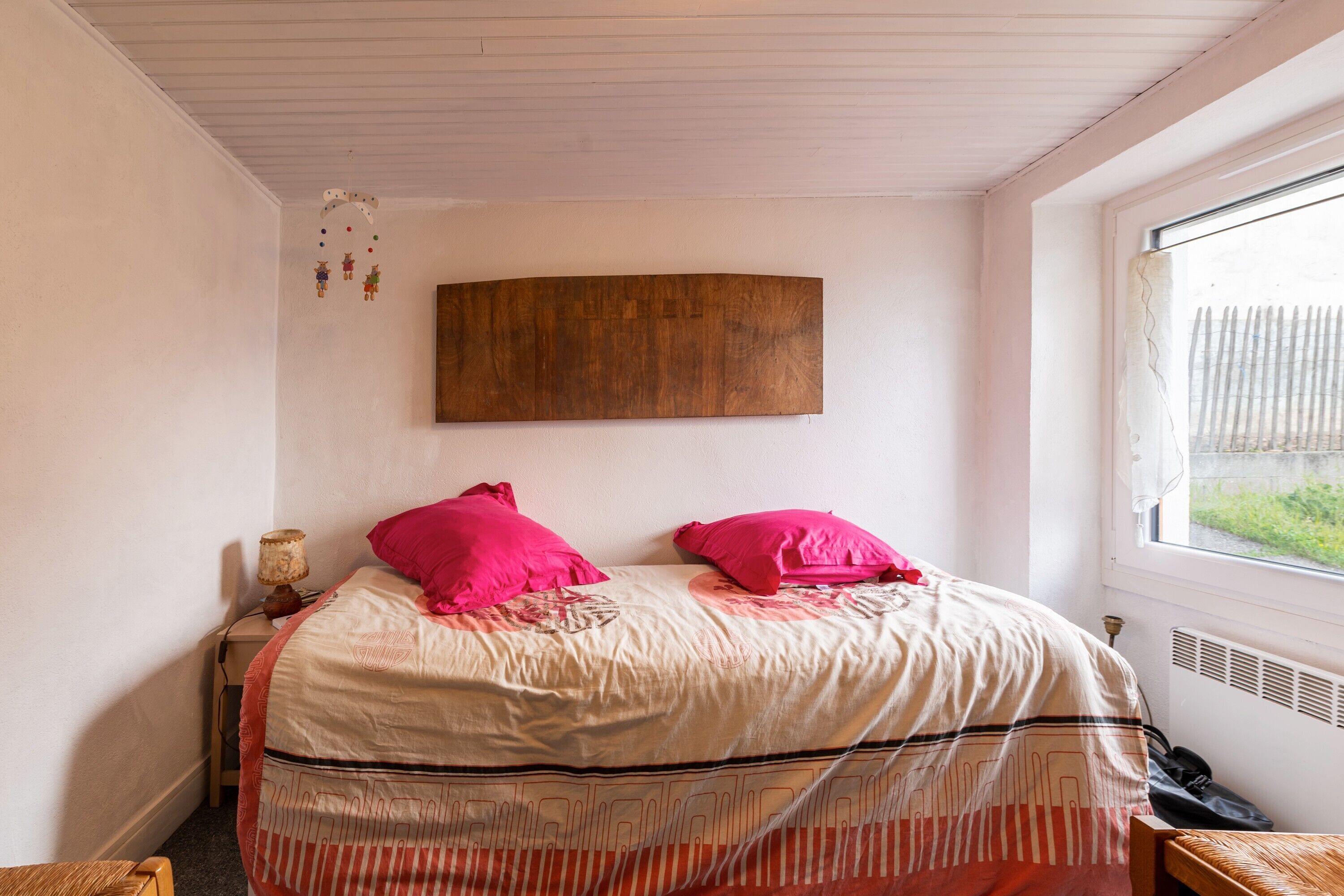 A bedroom with a bed, pillows, a nightstand, a lamp, a window, and a wooden headboard.