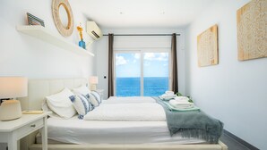 A hotel room with a bed, a nightstand, a lamp, a window with a view of the sea, and artwork on the walls. - Villa 'Azul' with Shared Pool, Wi-Fi and Air Conditioning (Cala Pi)
