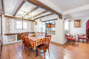 Un comedor con una mesa y sillas de madera, una cocina al fondo y una silla roja con cojín.