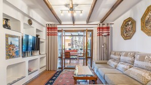 Un salón con sofá, televisión, estanterías y vistas a través de un ventanal.