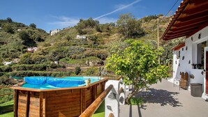 Ein Pool mit Holzterrasse, Steinmauer und Blick auf eine hügelige Landschaft.