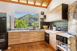 Une cuisine moderne avec des meubles en bois, un réfrigérateur noir, un mur d’accent en pierre et une vue sur un paysage montagneux.