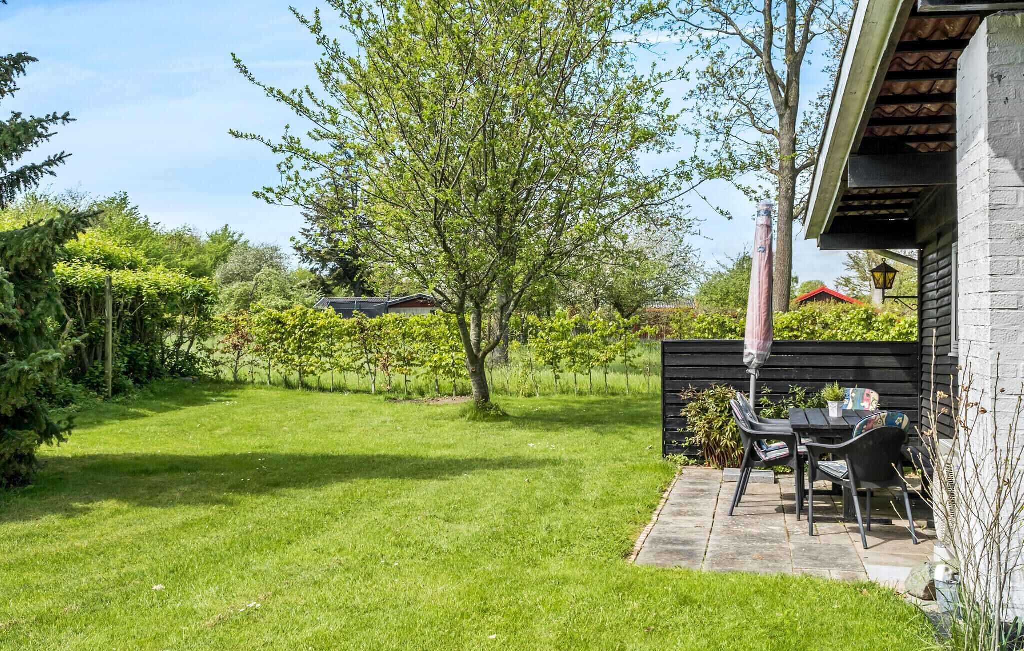 Ein gepflegter Garten mit Rasen, einem Baum und einer Terrasse mit Tisch und Stühlen.