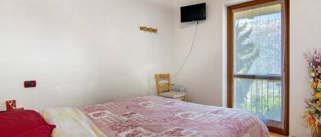 A bedroom with a bed, a television mounted on the wall, a window, and a chair.