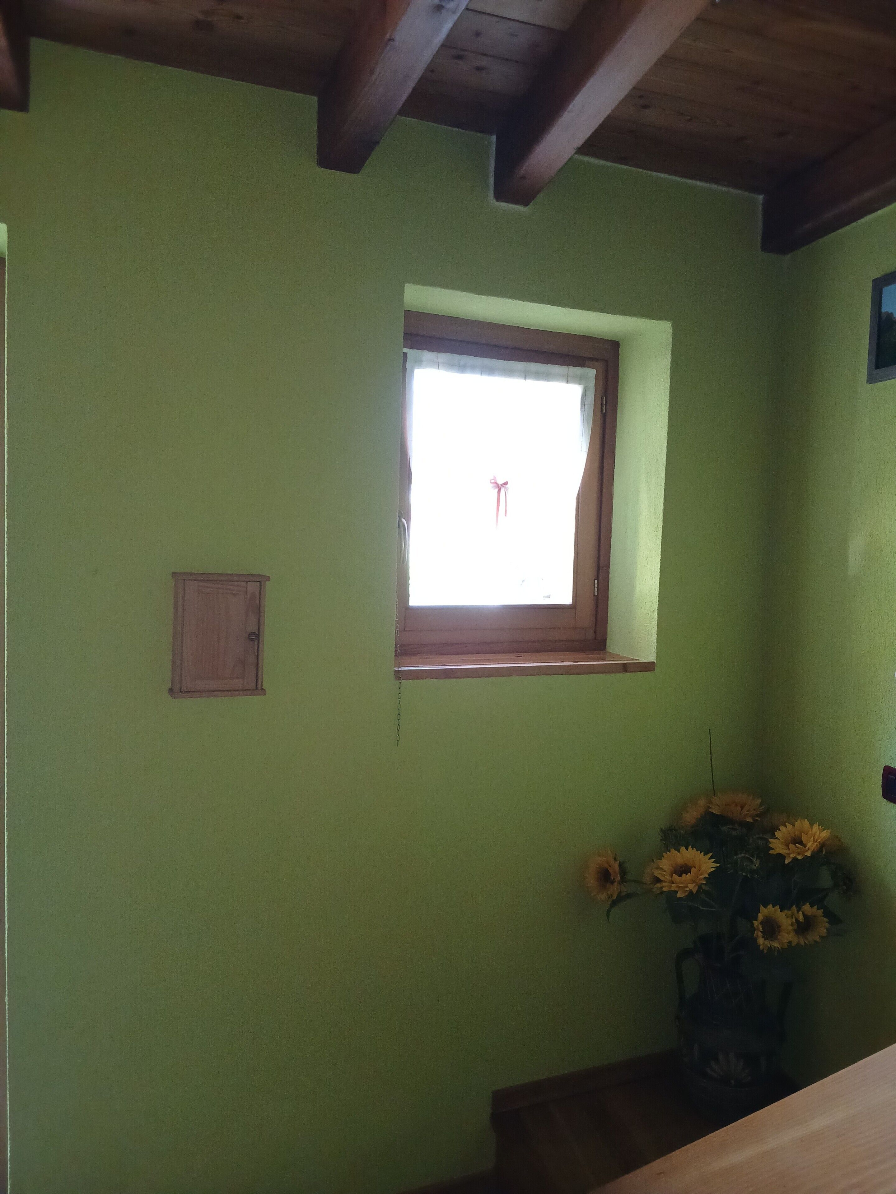 A room with a green wall, a small window, a wooden cabinet, and a vase with sunflowers.