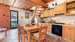 Een keuken met houten kastjes, een eettafel met stoelen, een fornuis en een koelkast.