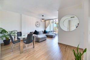 Un salon moderne avec une table à manger en verre, des canapés gris et un grand miroir.