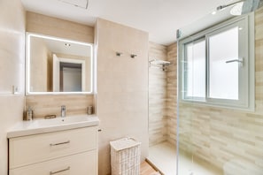 A modern bathroom with a large mirror, a sink, and a shower area.