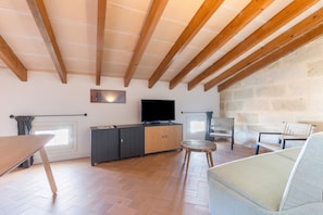 Une pièce avec un plafond en bois, un téléviseur posé sur un meuble, un canapé et une table.